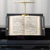 Notenständer mit geöffnetem Notenbuch auf Klavier, beleuchtet von einer goldenen Lampe.