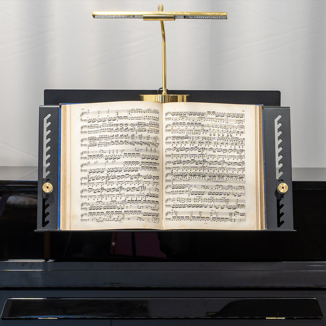 Notenständer mit geöffnetem Notenbuch auf Klavier, beleuchtet von einer goldenen Lampe.
