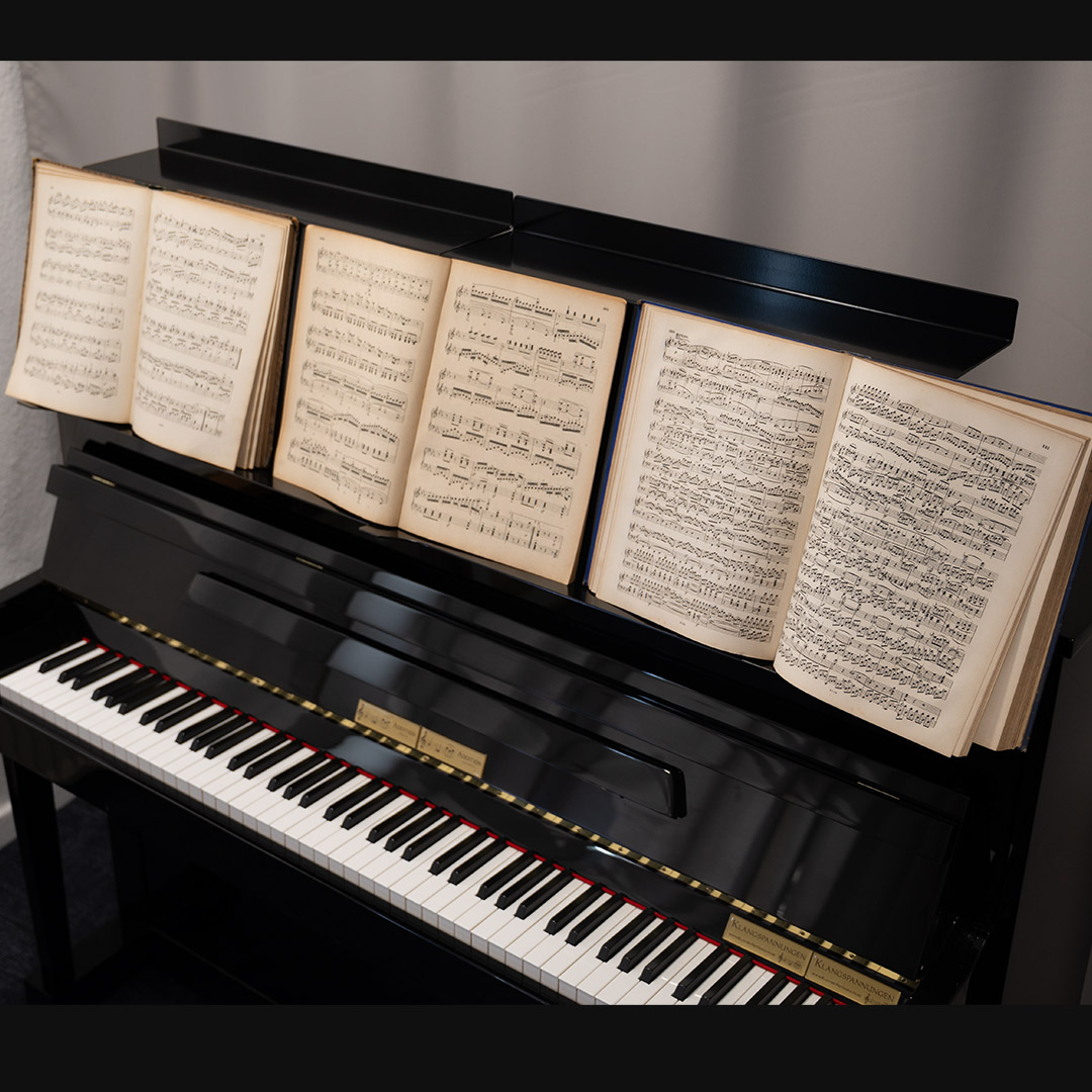 Schwarzes Klavier mit offenen Notenheften auf dem Notenständer.